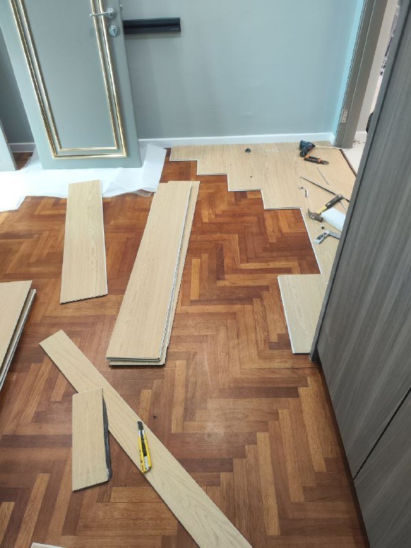 Old reddish-brown herringbone parquet timber floor in a Bloomsvale KL bedroom with new light oak SPC planks being laid beside it